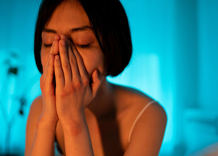 Woman with eyes closed and hands covering face, expressing emotion in a dimly lit room, reflecting on divorce revelations.