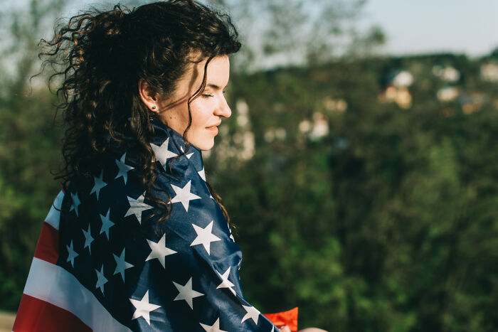 Young woman wrapped in an American flag outdoors, illustrating culture shock and reactions of foreigners experiencing new traditions.