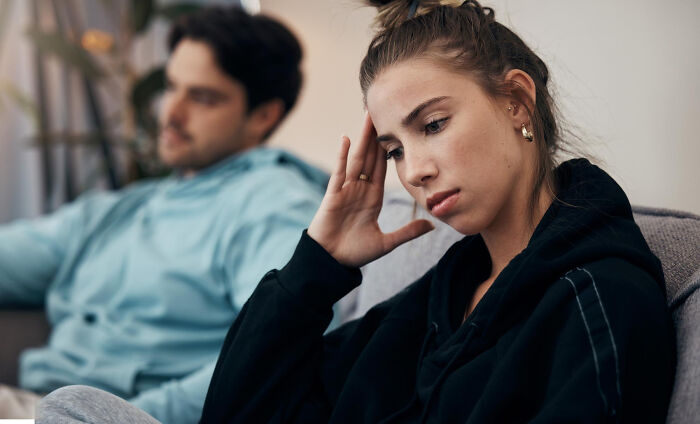Young woman looking upset and distant sitting on a couch with her partner, illustrating tough reasons in a relationship.