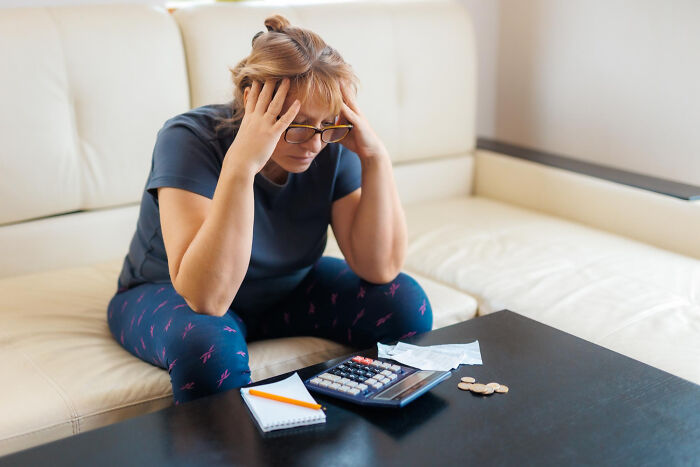 Stressed woman sitting on couch, struggling with finances, calculator, coins, and receipts on table symbolizing tough relationship reasons.