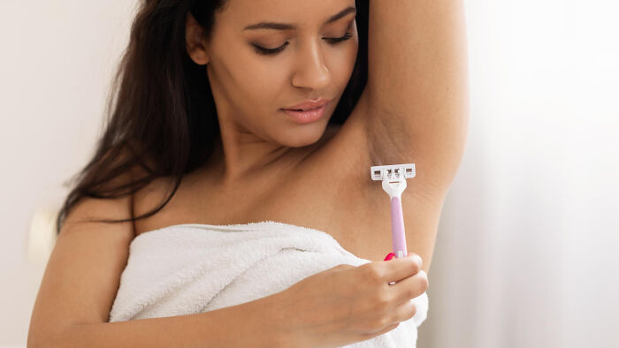 Woman in towel shaving underarm, illustrating personal care related to period wardrobe and women’s secrets.