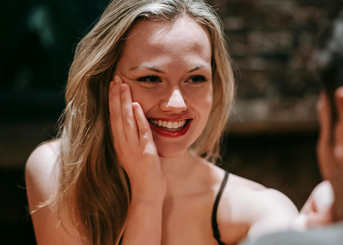 Smiling woman with hand on cheek engaged in a lively conversation, showcasing emotions in a messy love triangle moment.