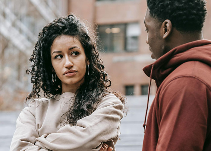 Uma mulher parece desconfiada enquanto conversa com um homem ao ar livre, ilustrando um momento de verdade e realização no relacionamento.