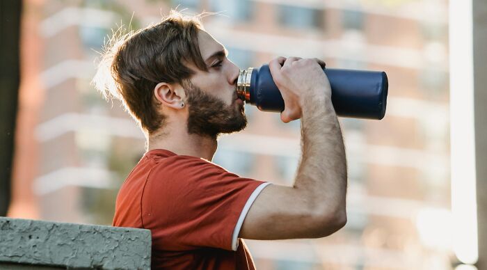 Young man drinking from a water bottle outdoors, representing reflection on ethical and moral dilemmas in everyday life.