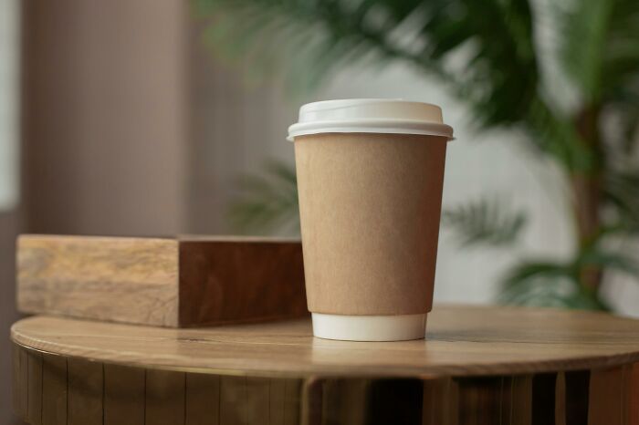 Disposable coffee cup with lid on wooden table in soft natural light, evoking thought-provoking ethical and moral dilemmas.