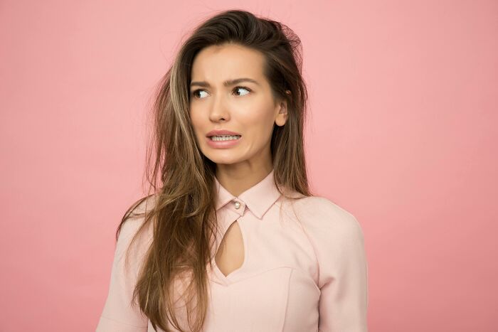 Young woman with long hair looking uneasy and uncertain against a pink background representing ethical dilemmas.