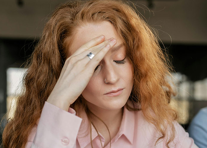 Mulher com cabelo ruivo e piercing no nariz tocando a testa, parecendo estressada enquanto reflete sobre o divórcio e ex revelando seu verdadeiro eu.