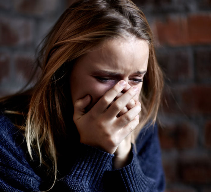 Young woman showing deep regret and emotional distress, covering her mouth with hands in a dark indoor setting.