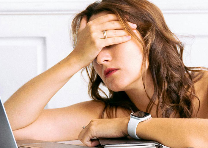 Woman wearing smartwatch looking stressed and frustrated while resting her head on her hand near a laptop, illustrating happily divorced moments.