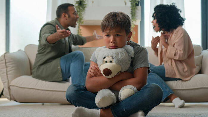 Child holding a teddy bear looking upset while parents argue in the background illustrating tough reasons in a relationship.