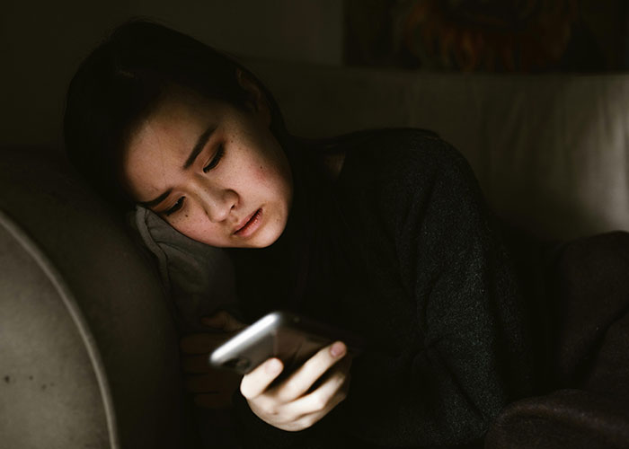 Young woman lying on couch looking distressed while holding phone, reflecting effects of nagging to lose weight.