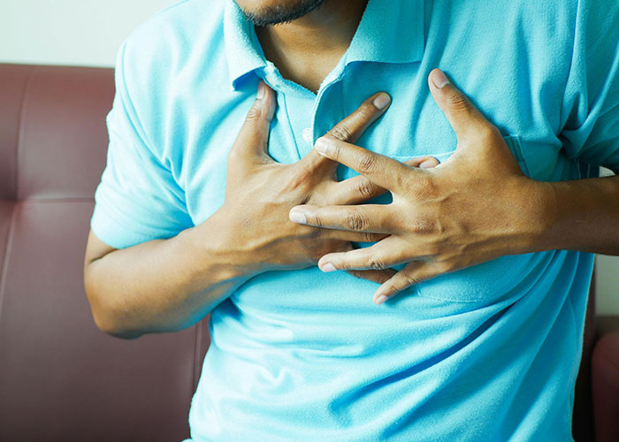 Man in a blue shirt clutching his chest in pain, illustrating unserious reasons for ending up in ER visits.