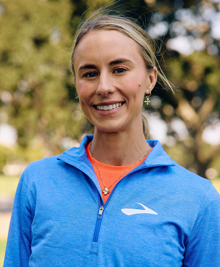 Female US track star in blue jacket smiling outdoors, symbolizing the impact of officials’ mistake on her title fate.