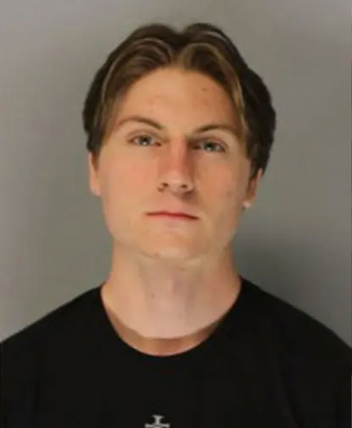 Young man with serious expression in a black shirt, linked to students prank on teacher tragedy and family decision.