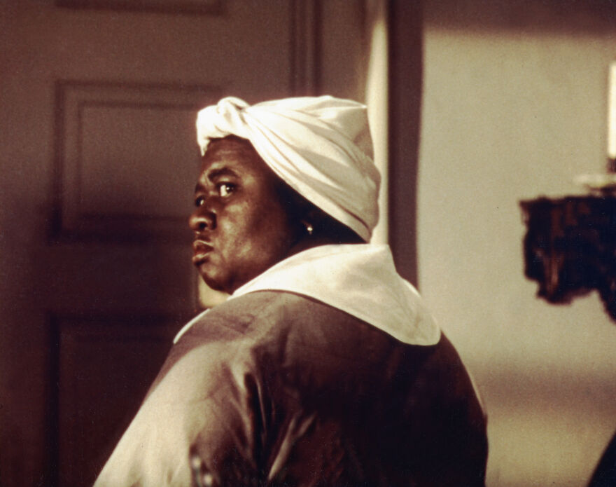 Hattie McDaniel no filme E o Vento Levou com fantasia e lenço branco na cabeça, representando a primeira negra a ganhar um Oscar na história do cinema.