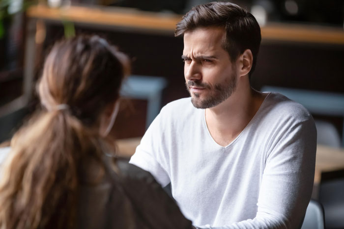 Man with a serious expression sharing a difficult conversation about a tumour with a woman in a quiet indoor setting.