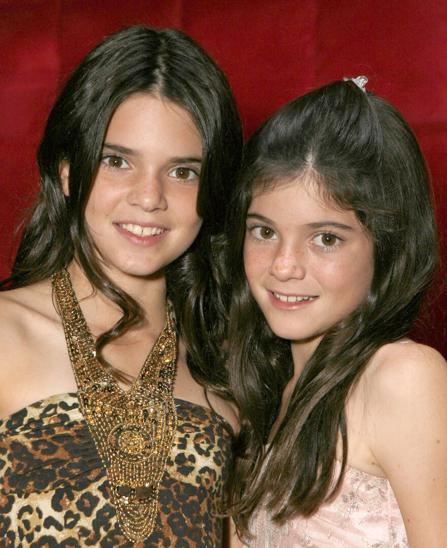 Kendall Jenner and Kylie Jenner with dark hair posing closely against a red background, showing natural looks before procedures.