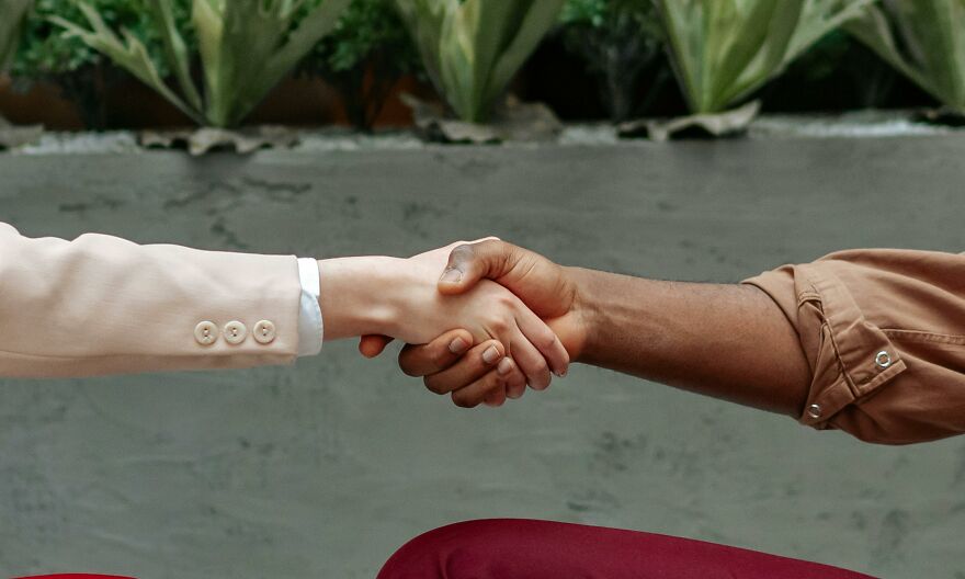 Two people shaking hands demonstrating small behaviors that make people like you more according to psychologists.