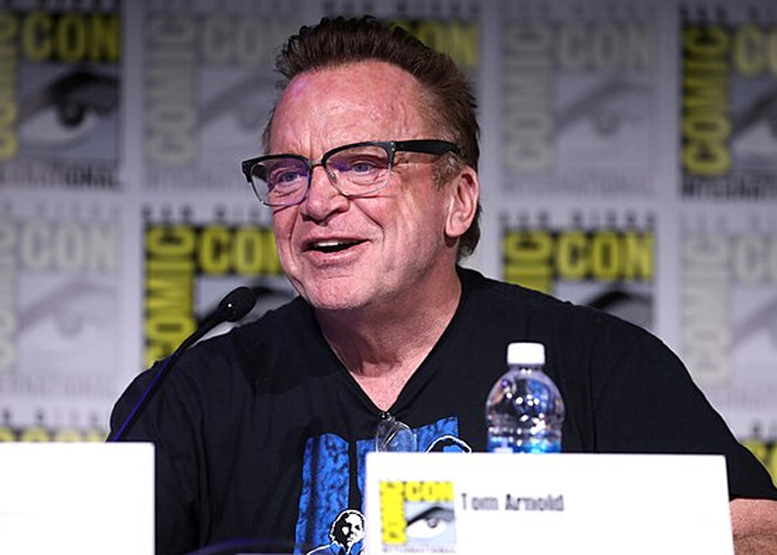 Man speaking at Comic-Con panel, wearing glasses and black shirt, illustrating celebrity encounters with raging jerks.