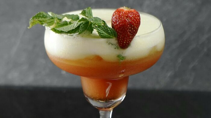 Cocktail glass with frothy drink garnished with fresh mint and a ripe strawberry.