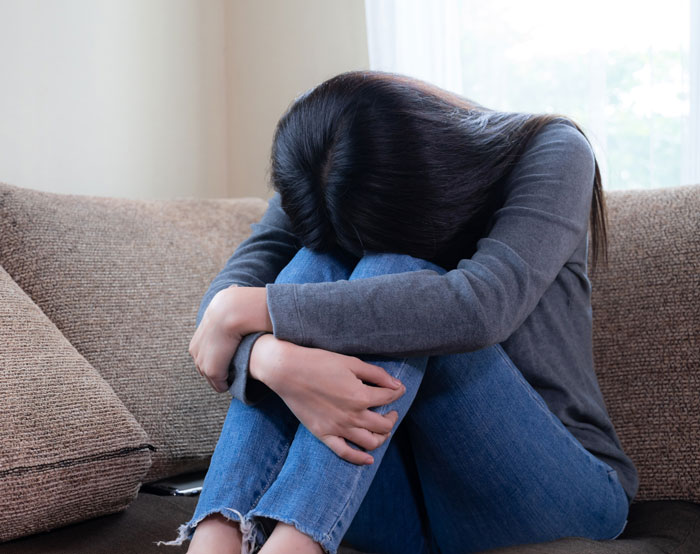 Woman sitting on a couch with head down, showing deep regret after ditching fianc&eacute;e to chase the one that got away.