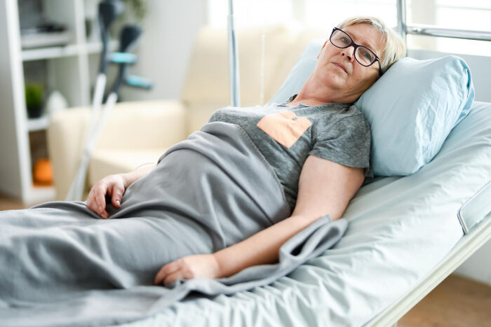 Elderly woman lying in hospital bed, appearing unwell, representing cases of patients faking illness in medical settings.