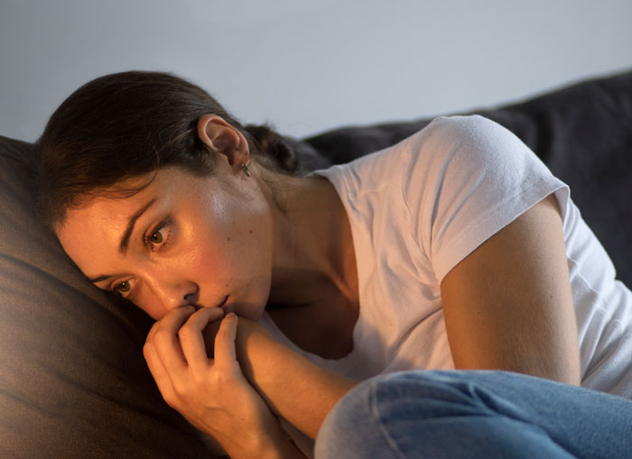 Woman lying on couch looking distressed after cutting off parents following betrayal involving mom and fiancé.