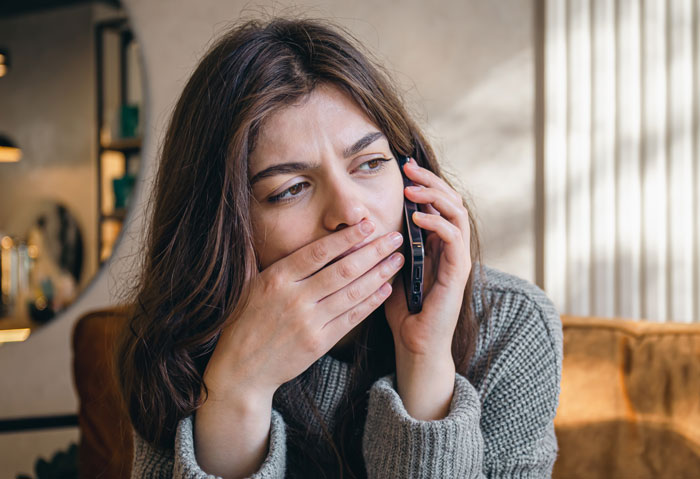 Woman with long brown hair looking regretful while talking on the phone, reflecting deep regret in a cozy indoor setting.