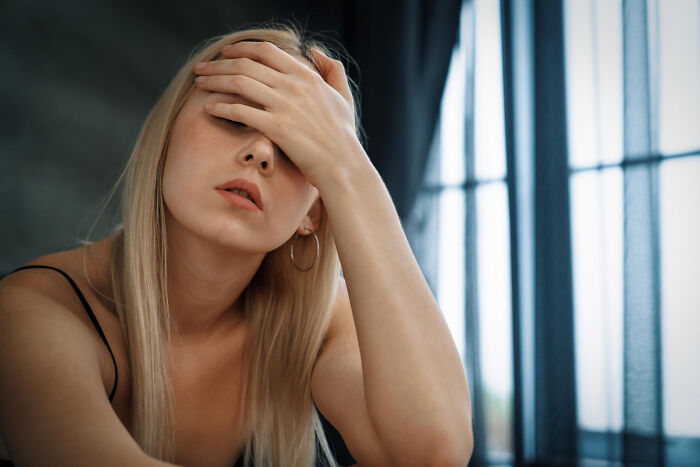 Woman sitting indoors with hand on forehead, expressing stress and frustration in a troubled relationship situation.