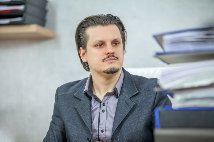 Man in gray suit sitting at desk surrounded by files, reflecting on Gen Z stare reactions and opinions.