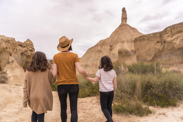 Three people holding hands, exploring a desert landscape with unusual rock formations and bizarre encounters visible.