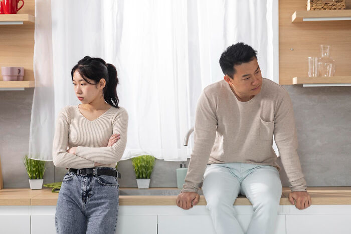 Couple avoiding eye contact in kitchen, depicting emotional distance in a relationship despite ongoing challenges.