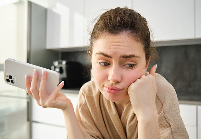 Woman looking upset and frustrated at home holding phone, reflecting on cutting off parents after catching mom with fiancé.