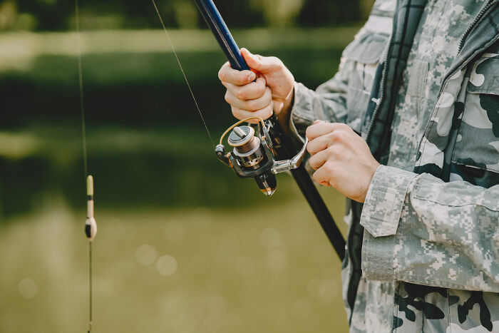 Person in camouflage jacket holding a fishing rod by a lake, part of bizarre encounters that left folks questioning what they saw.