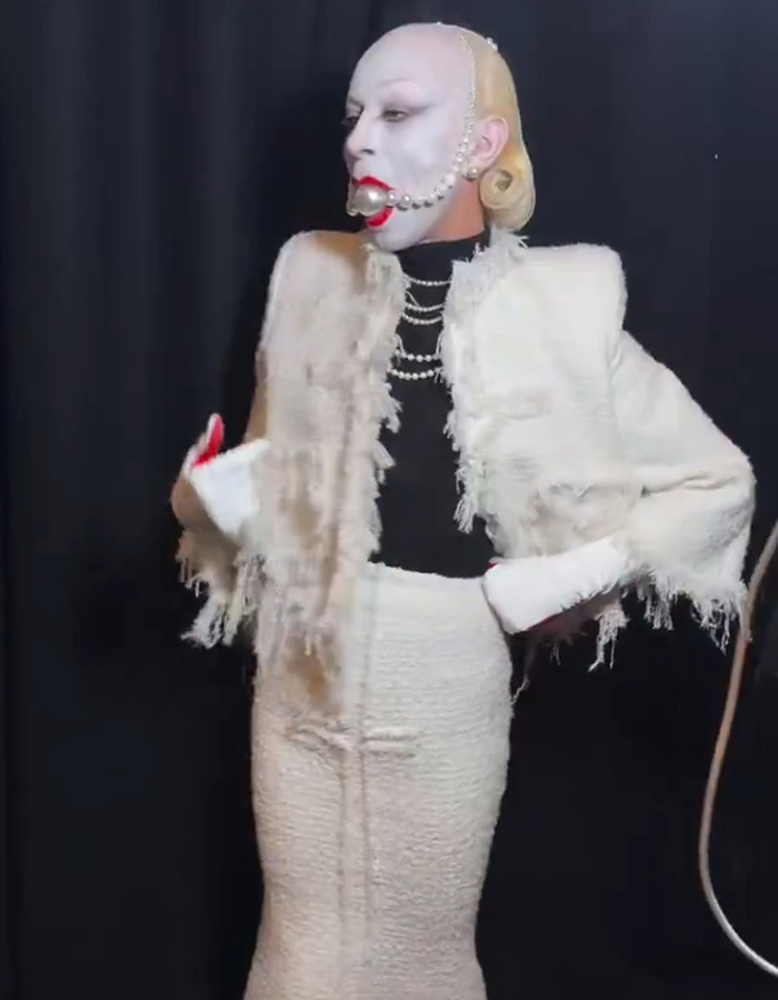 Model wearing avant-garde Paris Fashion Week outfit inspired by The Hunger Games, with white textured fabric and bold makeup.