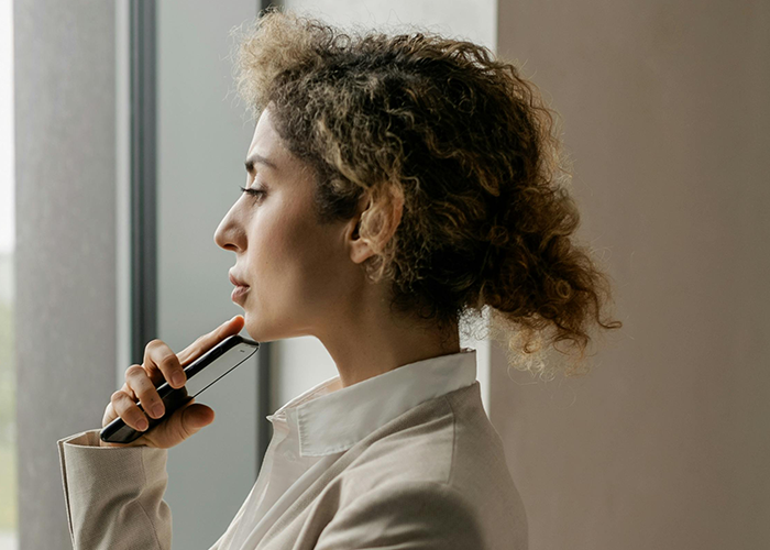 Young woman holding a phone, looking out a window, reflecting on a cheater hiding a one night stand secret.
