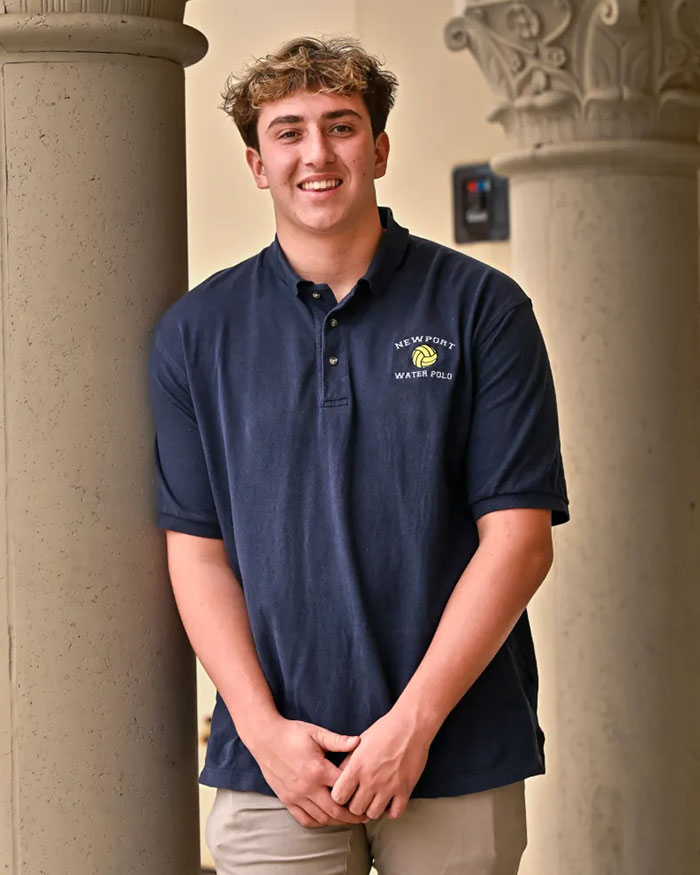Young star water polo player in navy Newport Water Polo shirt smiling confidently while standing between ornate columns. Young star water polo player in navy Newport Water Polo shirt smiling confidently while standing between ornate columns.