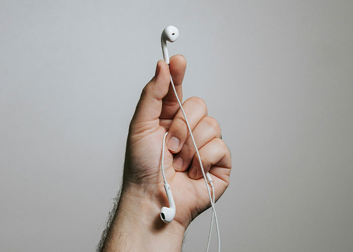 Hand holding white earbuds against plain background, illustrating major airline rule that draws passenger support.