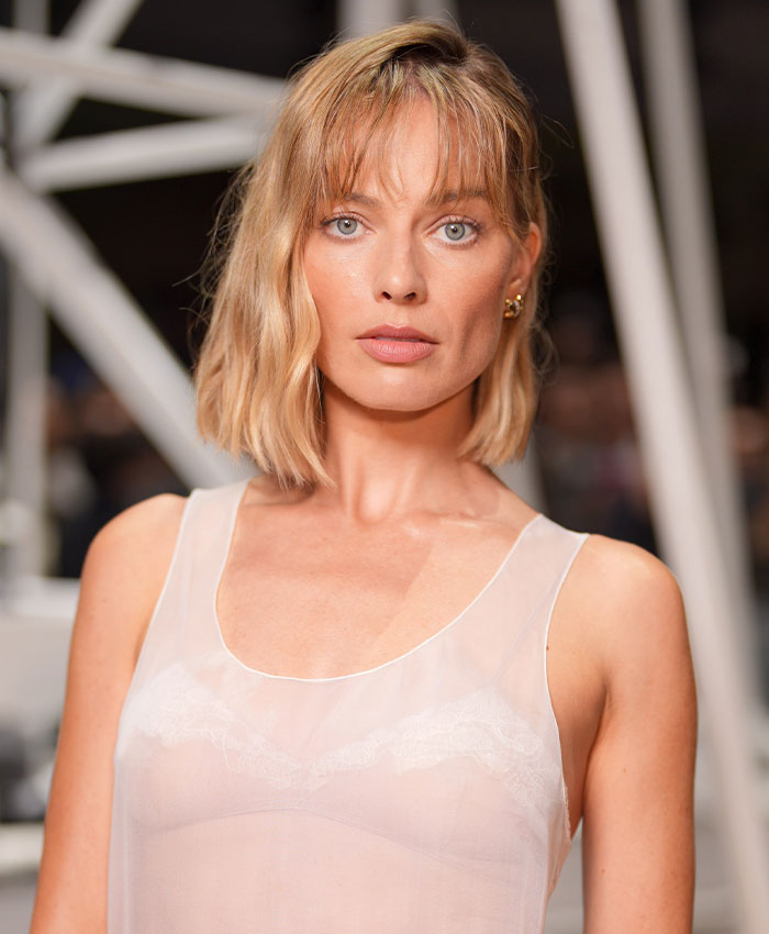 Margot Robbie at Paris Fashion Week wearing a sheer white top with mixed reactions during Hollywood event.