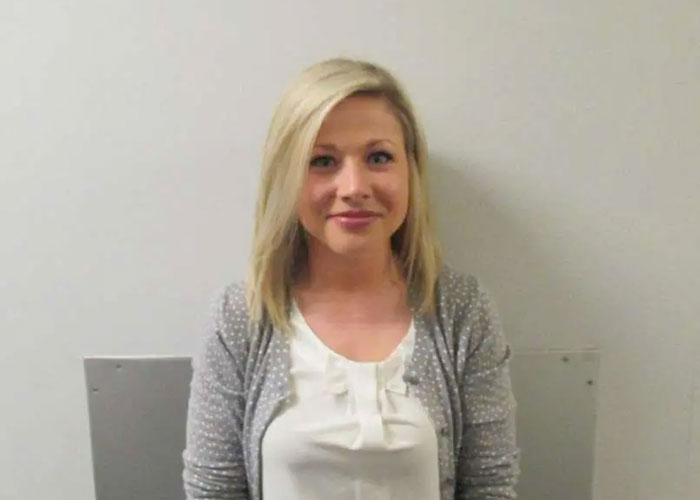 Teacher who went viral for smiling in her mugshot posing against a plain background after student scandal news.