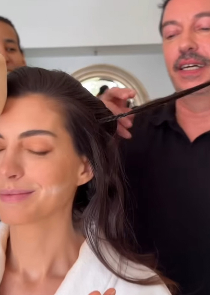 Anne Hathaway com os olhos fechados enquanto uma estilista cuida de seu cabelo revelando truques por trás do rosto tenso.