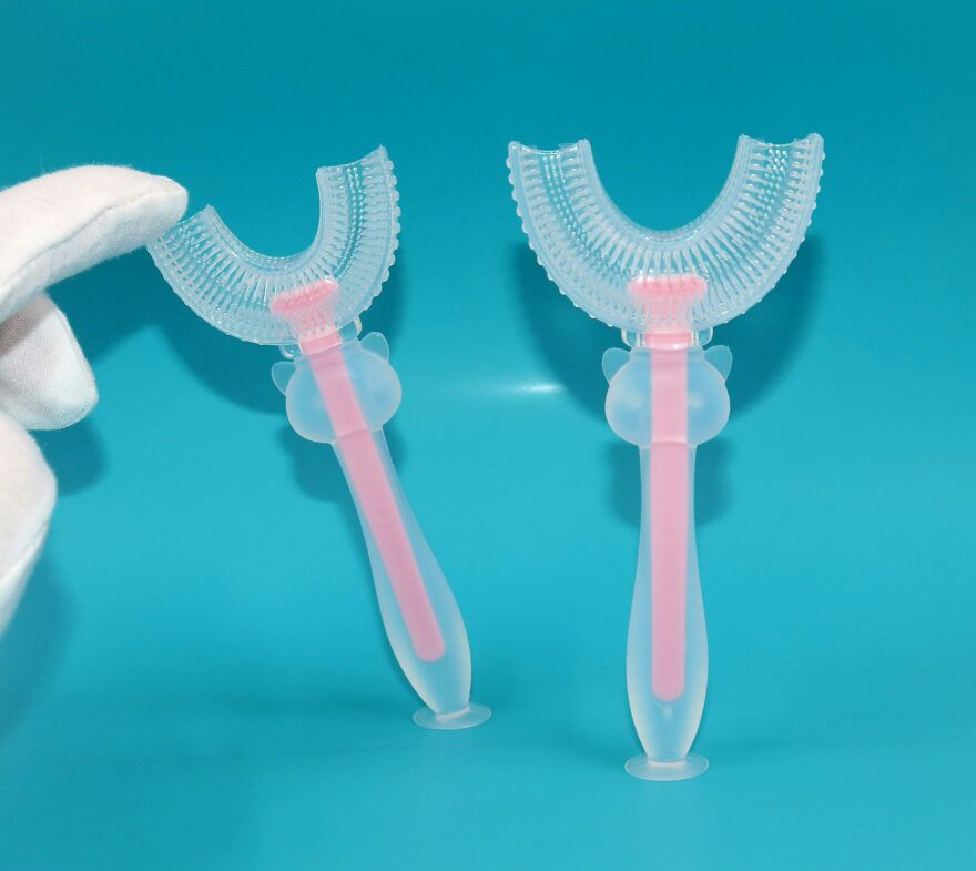 Curious objects showing two silicone toothbrushes with pink handles against a blue background with a gloved hand.