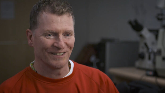 Man in red shirt smiling in a dimly lit room, illustrating crazy things people did for love in a casual setting.