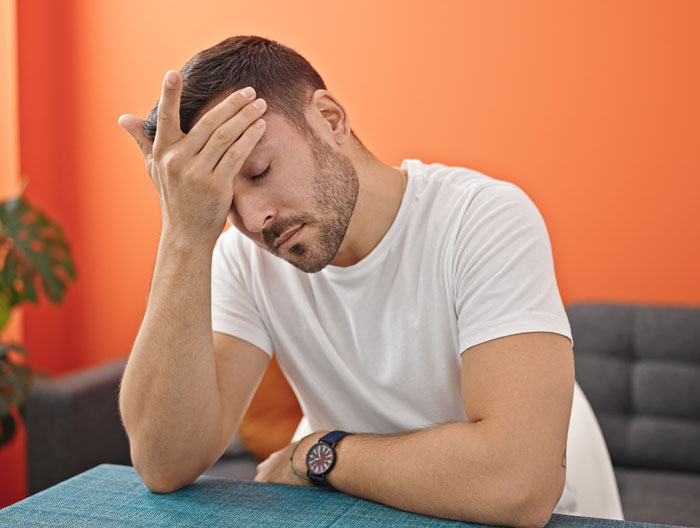 Man sitting at table with hand on forehead looking stressed over grandparents guilt trip involving his kid and mom