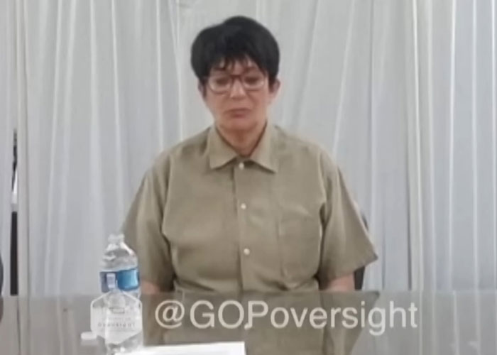 Ghislaine Maxwell sitting at a table in prison attire with water bottle during prison feud discussions and hygiene issues.