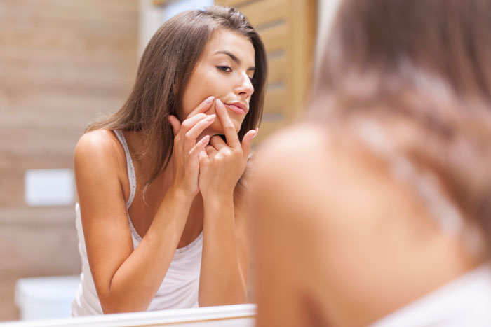 Young woman examining her face in the mirror, reflecting on weird and adorable relationship lessons about men.