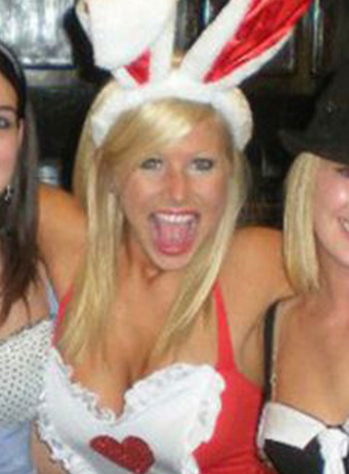 Blonde woman wearing bunny ears headband, smiling widely with friends in a festive party setting, viral teacher mugshot update.