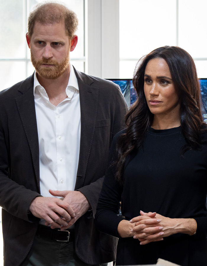 Prince Harry and Meghan standing side by side indoors with serious expressions after bombshell claims emerge