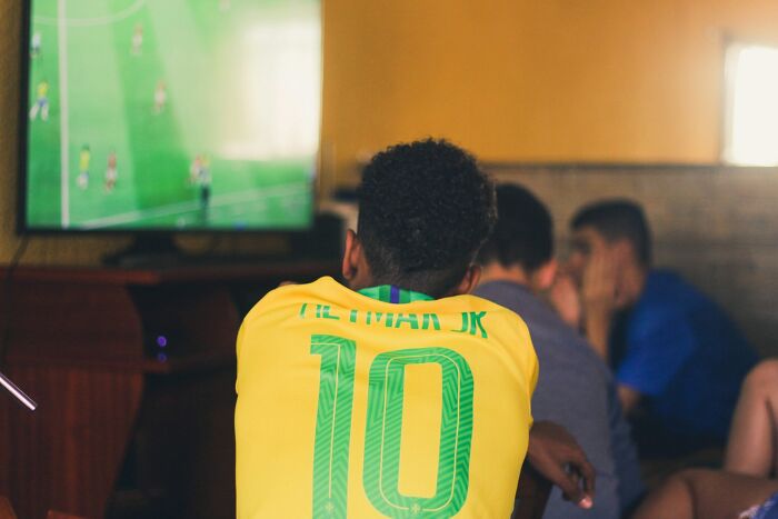 Young man wearing a Brazil soccer jersey watching a game on TV, reflecting on vanished truths from home countries.