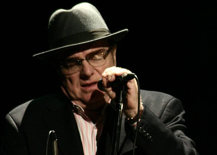 Man wearing hat and glasses, singing into a microphone on stage, illustrating celebrities who turned out to be raging jerks.